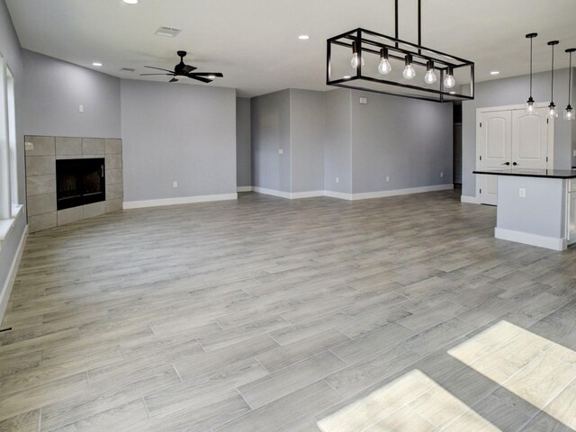 unfurnished living room with a tiled fireplace, light wood-type flooring, and ceiling fan