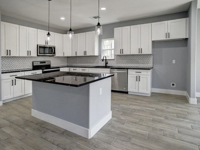 kitchen with sink, a center island, stainless steel appliances, decorative light fixtures, and white cabinets