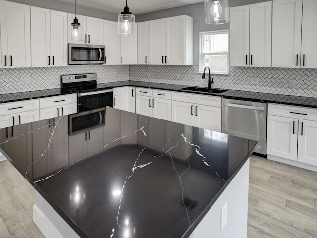 kitchen with white cabinetry, hanging light fixtures, stainless steel appliances, sink, and dark stone countertops