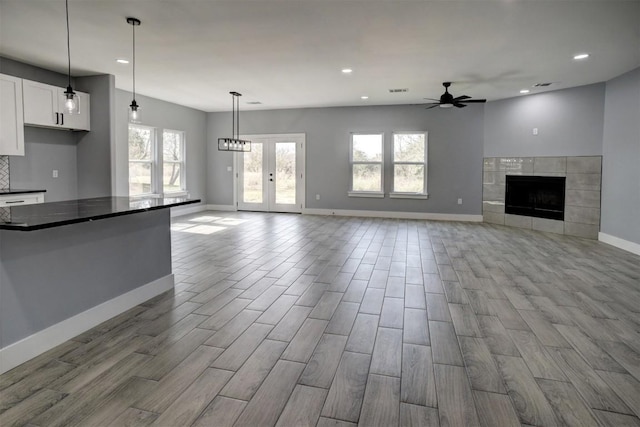 unfurnished living room with ceiling fan, light wood-type flooring, and a tiled fireplace