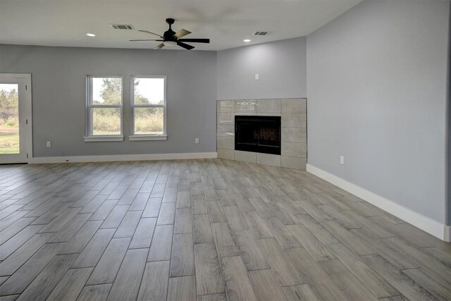 unfurnished living room featuring a tiled fireplace, ceiling fan, and light hardwood / wood-style flooring