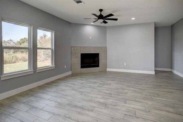 unfurnished living room with ceiling fan, a tile fireplace, and light hardwood / wood-style floors