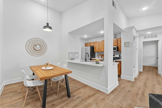 kitchen featuring light hardwood / wood-style floors, kitchen peninsula, appliances with stainless steel finishes, tasteful backsplash, and decorative light fixtures