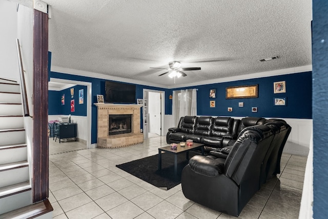 living room featuring ceiling fan, a textured ceiling, light tile patterned floors, and a brick fireplace