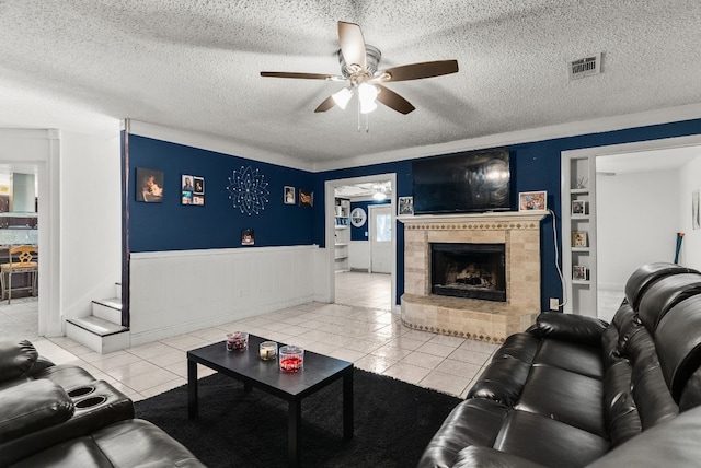 tiled living room featuring built in shelves, a tiled fireplace, a textured ceiling, and ceiling fan