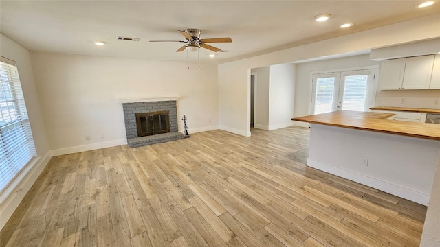 unfurnished living room featuring light hardwood / wood-style flooring, a brick fireplace, and ceiling fan