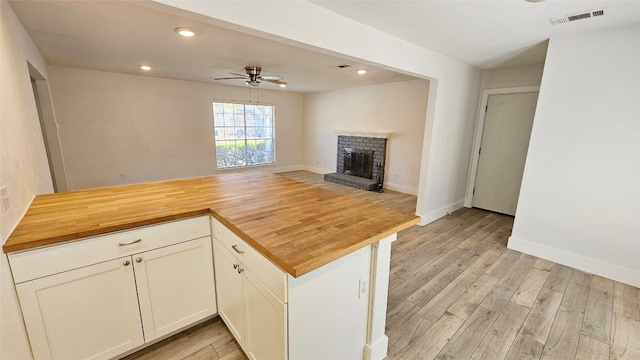 kitchen with light hardwood / wood-style flooring, white cabinetry, ceiling fan, and a brick fireplace