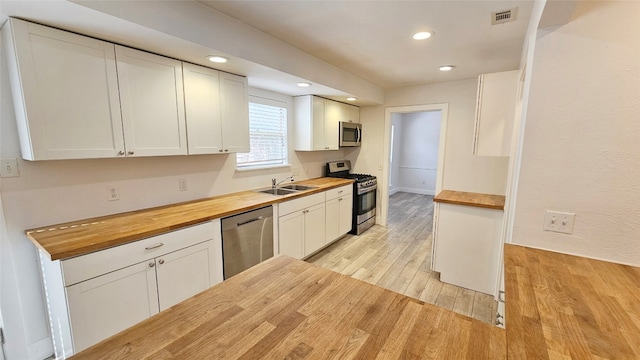 kitchen featuring white cabinets, appliances with stainless steel finishes, butcher block counters, light hardwood / wood-style floors, and sink