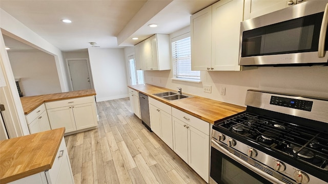 kitchen with butcher block countertops, stainless steel appliances, white cabinets, and light hardwood / wood-style floors