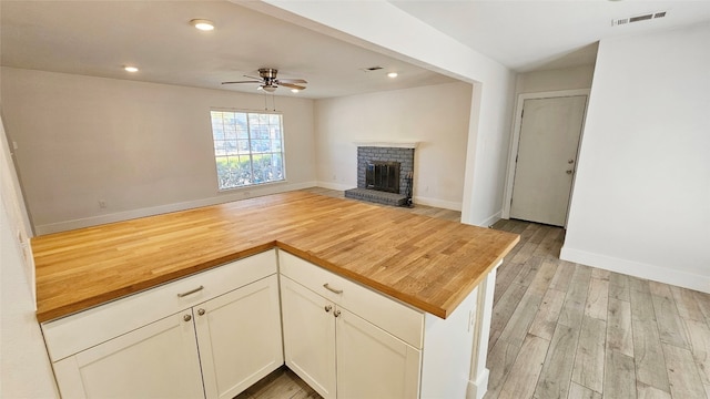 kitchen featuring butcher block countertops, white cabinets, a fireplace, light hardwood / wood-style floors, and ceiling fan