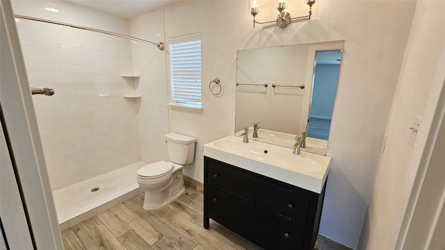 bathroom featuring vanity, a tile shower, wood-type flooring, and toilet