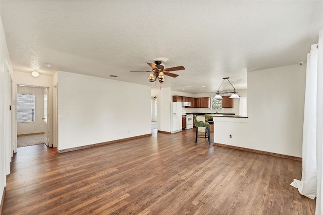 unfurnished living room featuring dark wood-type flooring, ceiling fan, and a textured ceiling