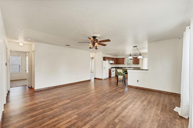 unfurnished living room with ceiling fan, dark hardwood / wood-style floors, a wealth of natural light, and a textured ceiling