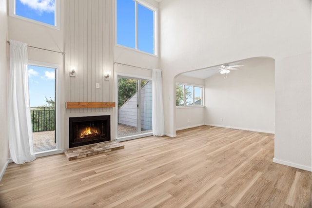 unfurnished living room featuring light wood-type flooring, a towering ceiling, and ceiling fan