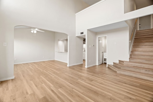 unfurnished living room featuring a towering ceiling, ceiling fan, and light hardwood / wood-style floors