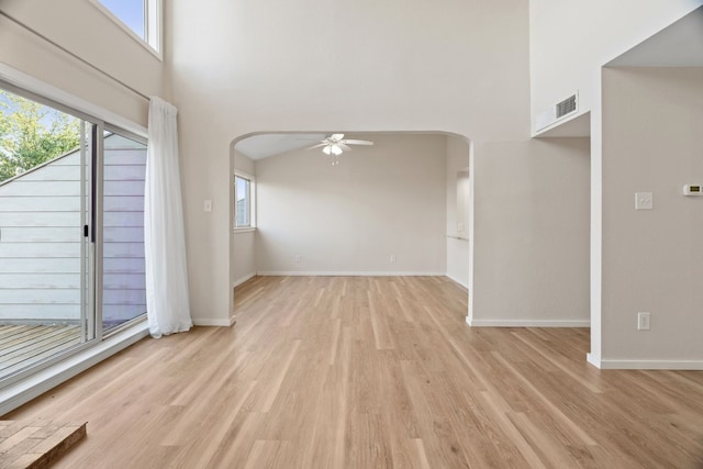 spare room with a towering ceiling, light hardwood / wood-style flooring, a healthy amount of sunlight, and ceiling fan