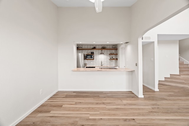 bar with appliances with stainless steel finishes, light hardwood / wood-style flooring, a towering ceiling, and ceiling fan