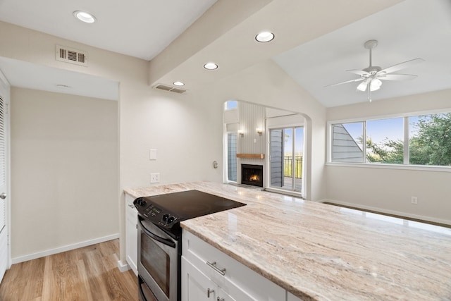 kitchen with light wood-type flooring, stainless steel electric stove, ceiling fan, white cabinets, and light stone counters