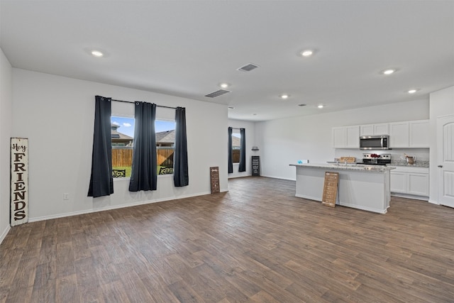 kitchen featuring a kitchen island with sink, dark hardwood / wood-style floors, light stone countertops, white cabinetry, and appliances with stainless steel finishes