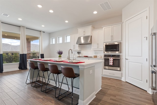 kitchen featuring white cabinetry, hardwood / wood-style floors, appliances with stainless steel finishes, and a center island with sink