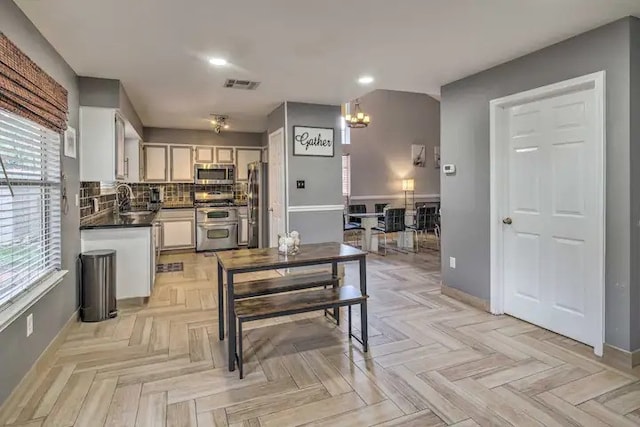 kitchen with stainless steel appliances, backsplash, sink, light parquet floors, and white cabinets