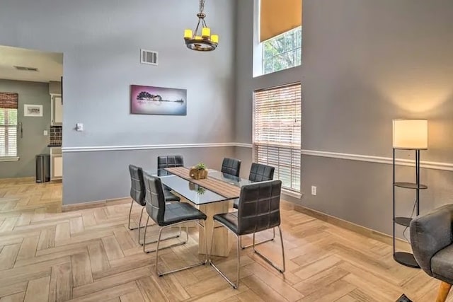 dining room with light parquet floors, a towering ceiling, and an inviting chandelier