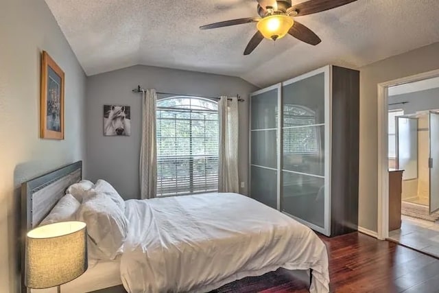 bedroom featuring dark hardwood / wood-style floors, ensuite bath, vaulted ceiling, a textured ceiling, and ceiling fan