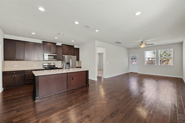 kitchen with stainless steel appliances, dark brown cabinetry, dark hardwood / wood-style floors, and a kitchen island with sink