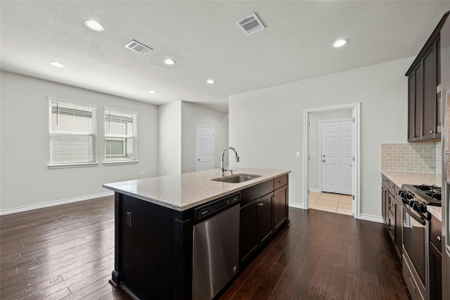 kitchen with appliances with stainless steel finishes, a kitchen island with sink, sink, and dark wood-type flooring