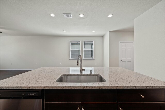 kitchen featuring stainless steel dishwasher, sink, a kitchen island with sink, and light stone countertops