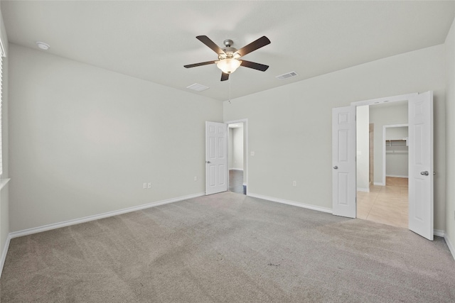 unfurnished bedroom with a spacious closet, ceiling fan, light carpet, and a closet