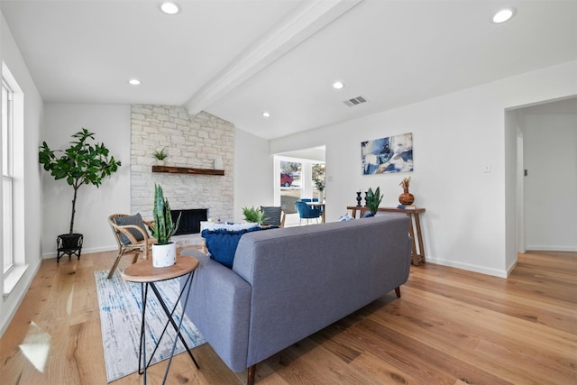 living room featuring vaulted ceiling with beams, light hardwood / wood-style flooring, and a stone fireplace