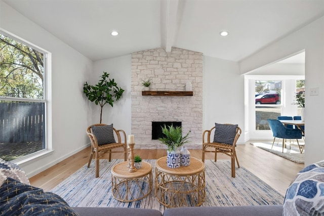 living room featuring vaulted ceiling with beams, light hardwood / wood-style flooring, a stone fireplace, and a wealth of natural light