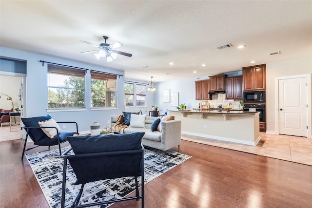 living room featuring a textured ceiling, sink, light hardwood / wood-style floors, and ceiling fan with notable chandelier