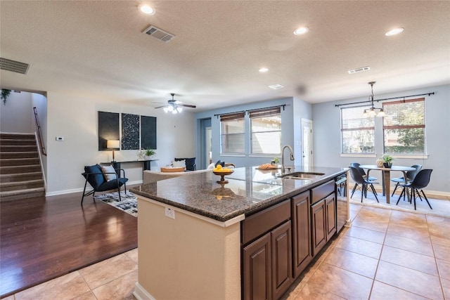 kitchen with pendant lighting, dark stone counters, sink, an island with sink, and light hardwood / wood-style floors