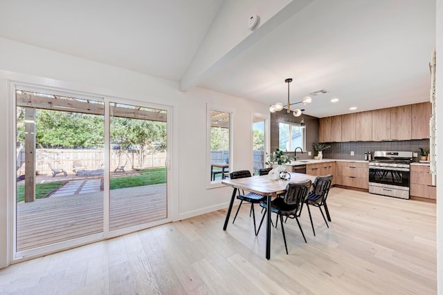 dining space featuring lofted ceiling, light wood-type flooring, a notable chandelier, and sink