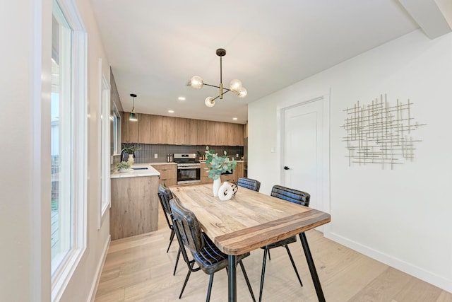 dining area with sink, a notable chandelier, and light wood-type flooring