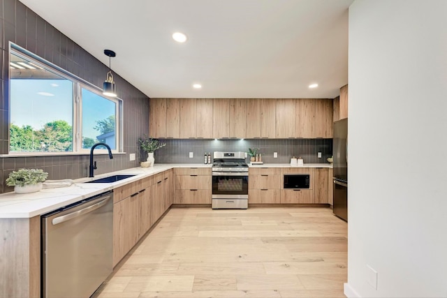 kitchen featuring appliances with stainless steel finishes, light wood-type flooring, sink, light brown cabinets, and decorative light fixtures