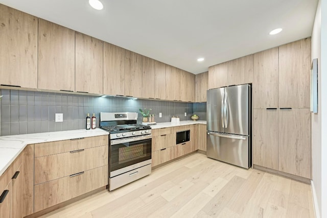 kitchen featuring decorative backsplash, light brown cabinetry, light stone counters, stainless steel appliances, and light hardwood / wood-style floors