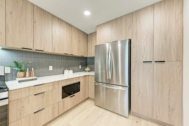 kitchen featuring light stone countertops, black microwave, stainless steel fridge, light hardwood / wood-style floors, and light brown cabinetry