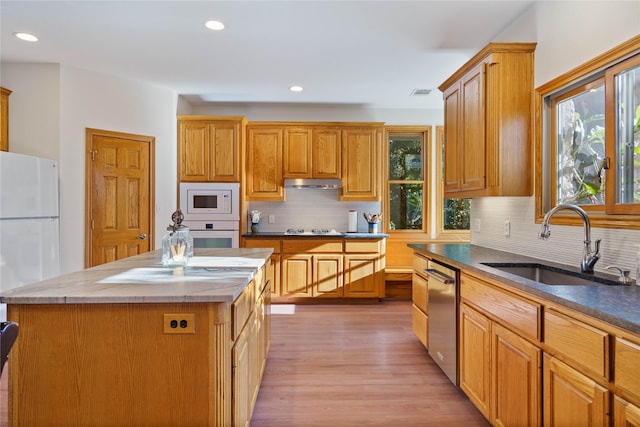 kitchen featuring white appliances, a kitchen island, sink, backsplash, and light wood-type flooring