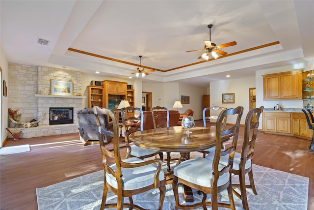 dining space featuring ceiling fan, a stone fireplace, a tray ceiling, and light hardwood / wood-style floors