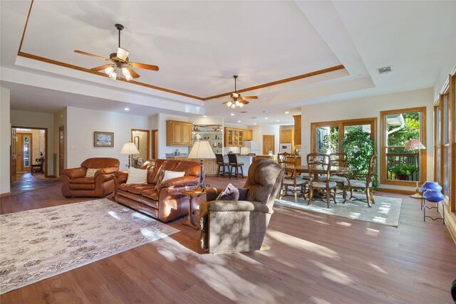 living room with ceiling fan, wood-type flooring, and a raised ceiling