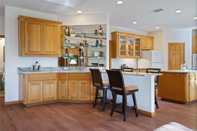 kitchen with kitchen peninsula, white refrigerator, dark hardwood / wood-style floors, and a breakfast bar