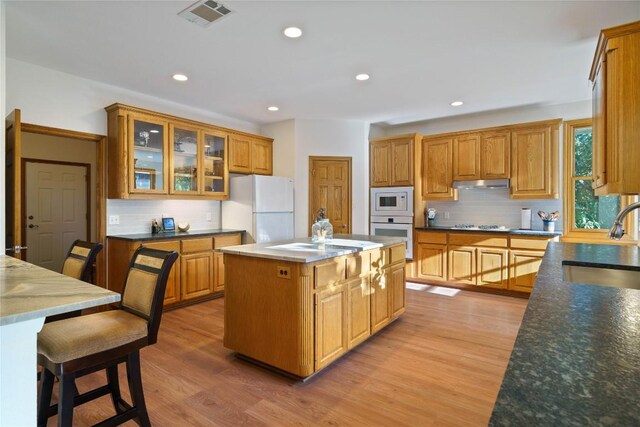 kitchen with white appliances, a center island, tasteful backsplash, light hardwood / wood-style floors, and sink