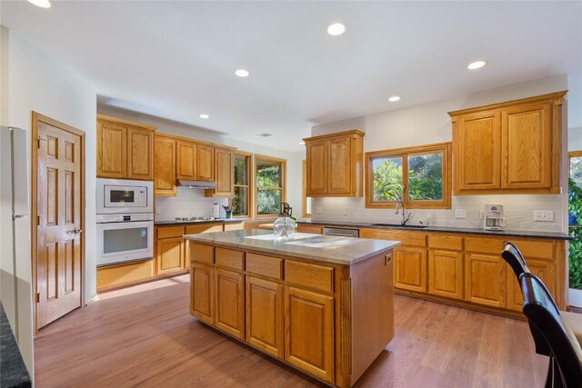 kitchen with tasteful backsplash, a center island, sink, light wood-type flooring, and appliances with stainless steel finishes