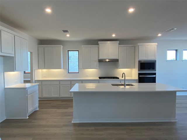 kitchen featuring dark hardwood / wood-style floors, built in microwave, white cabinetry, an island with sink, and sink