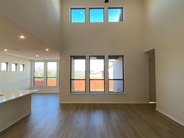 unfurnished living room featuring a towering ceiling, dark wood-type flooring, and ceiling fan