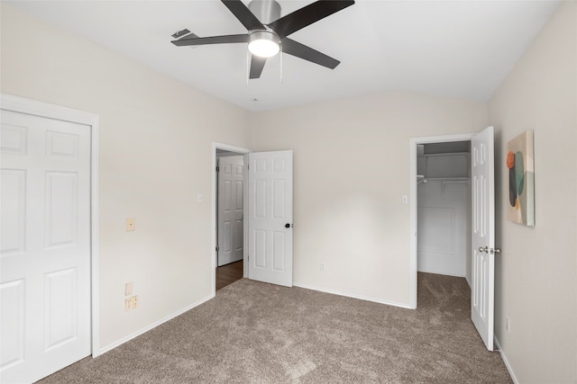 unfurnished bedroom with a walk in closet, vaulted ceiling, carpet, and ceiling fan