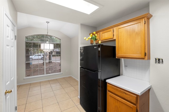 kitchen featuring black fridge, backsplash, light tile patterned flooring, vaulted ceiling, and decorative light fixtures